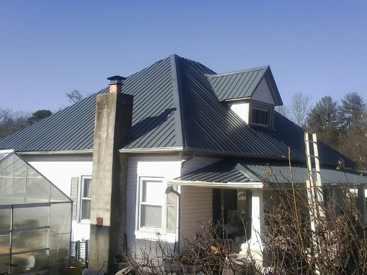 Dark blue standing seam metal roof on a white farmhouse with dormer — Slate & Tile Roof Repair by Roofing Brothers in Stewartsville