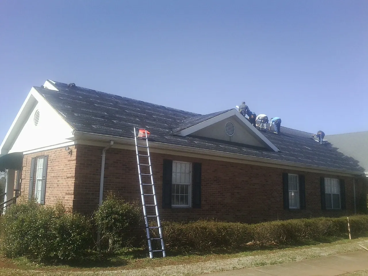 Crew tearing shingles off a brick ranch roof with a ladder set — Emergency Roof Repair work by our crew in Stewartsville