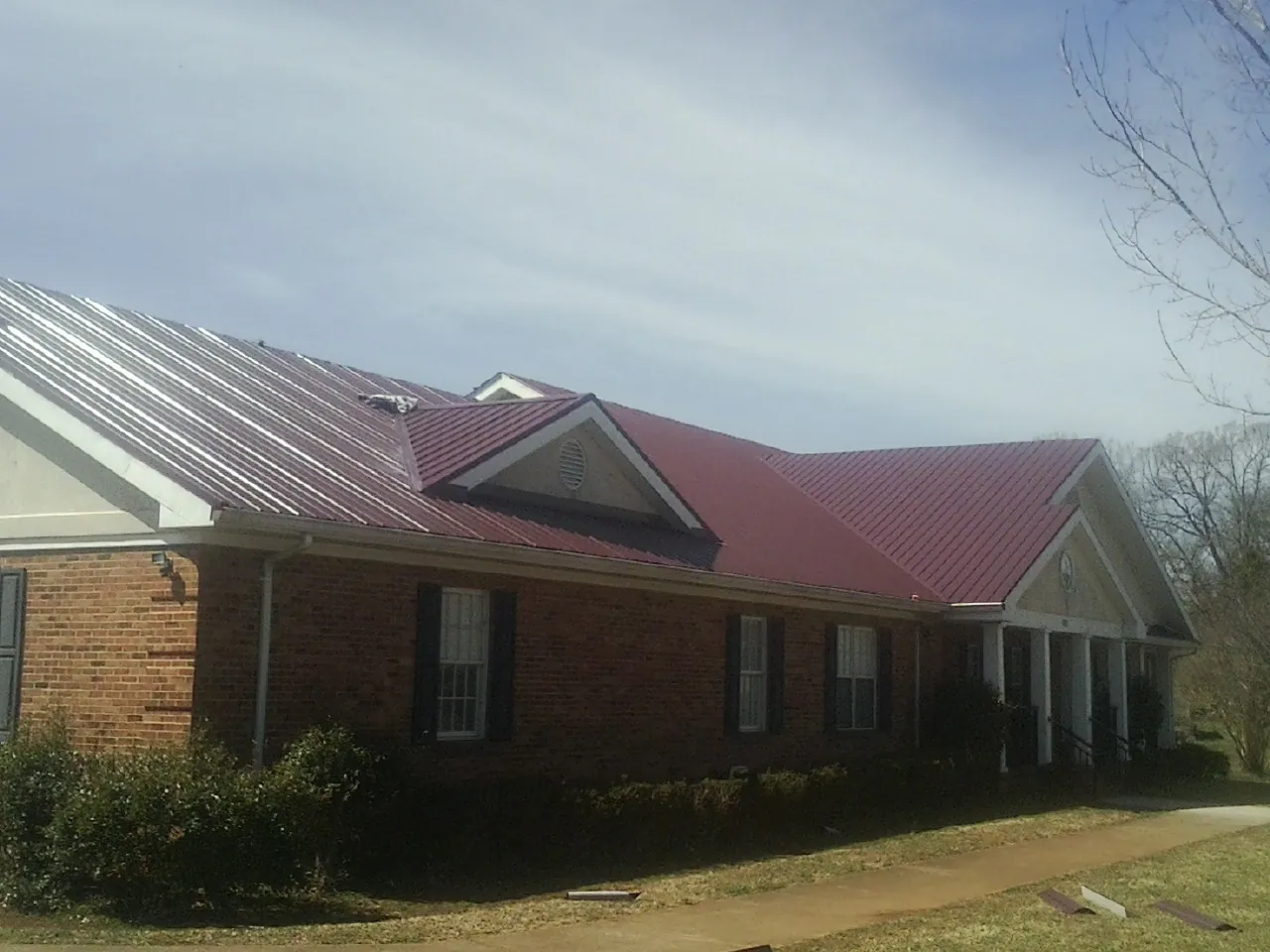 Red metal roof with gabled entries on a long brick building, from a Hail Damage Roof Repair job in Stewartsville