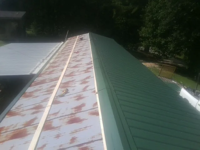 Old rusted panels beside newly installed green metal roofing — Wind Damage Roof Repair by Roofing Brothers in Stewartsville