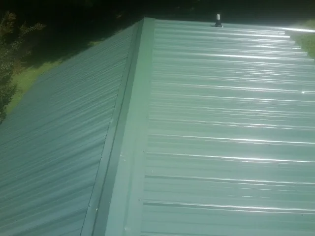 New green metal panels meeting at the ridge of a roof — Flat Roof Repair work by our crew in Stewartsville