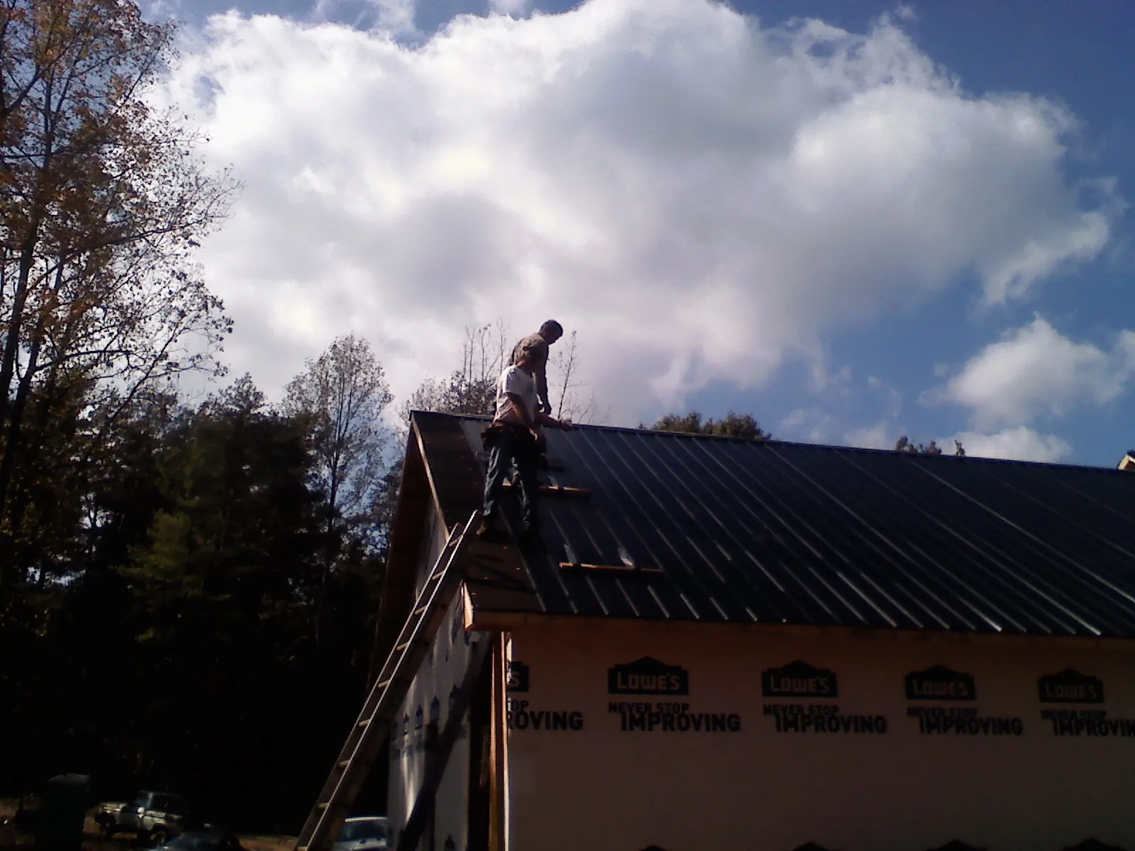 Roofer fastening dark metal panels high against a cloudy sky, from a Roof Inspection job in Stewartsville