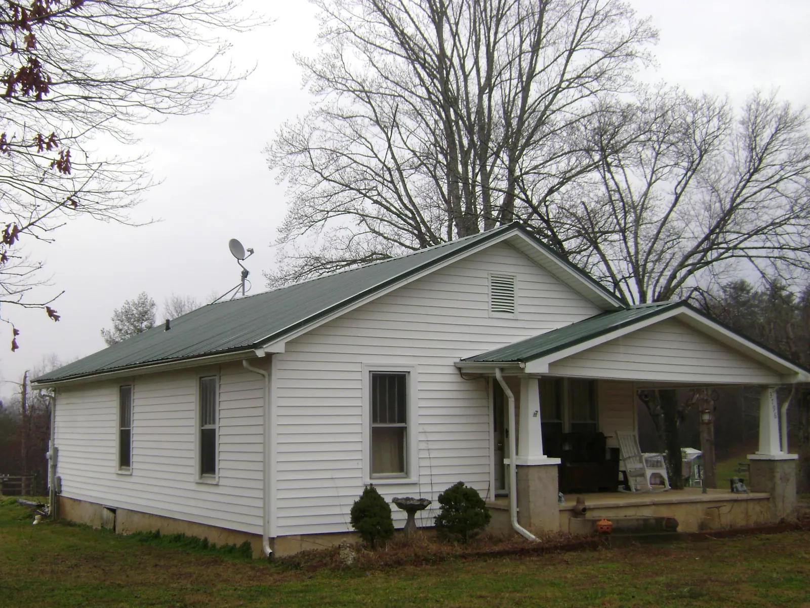 Green metal roof on a white bungalow with a side porch in Stewartsville